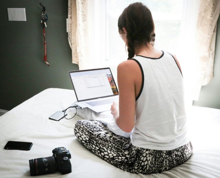 Eine Frau sitzt auf einem Bett und arbeitet an einem Laptop.