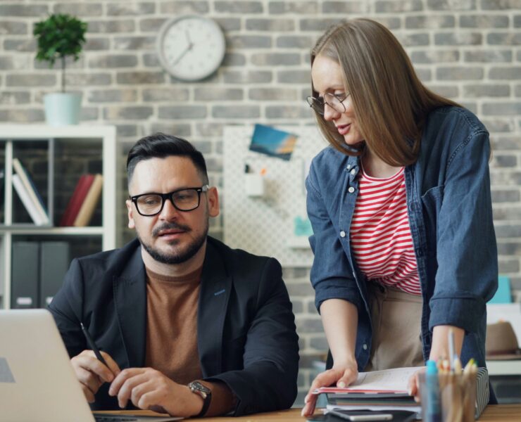 Dois colegas de trabalho olhando um para o outro em um laptop