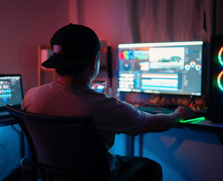 Ein Mann sitzt vor einem Computerbildschirm mit großen Lautsprechern und bearbeitet ein Video.