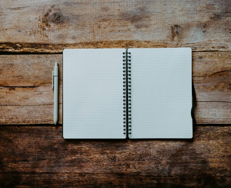Um caderno aberto com páginas em branco sobre uma mesa de madeira com uma caneta ao lado.