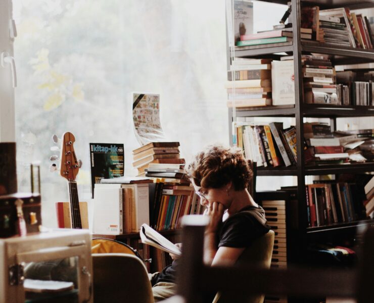 Uma mulher em uma sala cheia de livros, lendo suas anotações e pensando em como transformar ideias tediosas em uma ótima história.