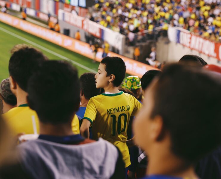 Un niño pequeño en un estadio viendo un partido de fútbol mientras lleva la camiseta de su jugador de fútbol favorito.