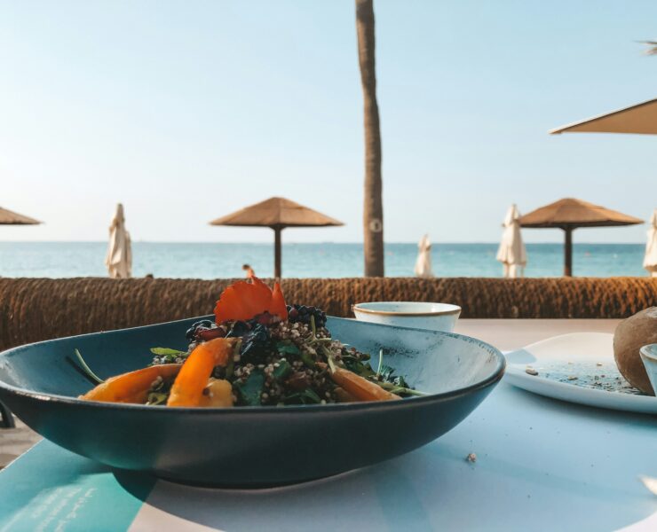 An image showing a mediterranean dish on a table with the beach in the background.